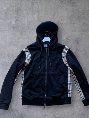 Burberry hoodie  - Burberry Nova Check Zip Hoodie  Exklusiv Burberry Nova Check Zip Hoodie i 10/10 skick. Klassisk Nova Check-design med zip och den ikoniska Burberry-känslan. Enda anmärkningen är att en stitch i huvudtaggen har släppt, vilket inte påverkar användningen.  • Burberry Nova Check • Zip hoodie • 10/10 skick • Endast en liten stitch i huvudtaggen är av • Nypris ca 10 000 kr  Skickas inom 24H📦