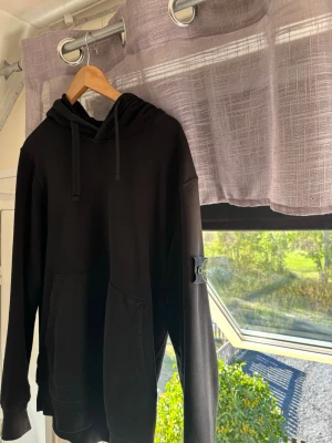 Svart hoodie med ficka och huva - Säljer en svart hoodie med klassisk känguruficka framtill och justerbar huva med snören. Hoodien har långa ärmar och ribbade muddar vid ärmslut och nederkant. Perfekt för en avslappnad och stilren look. Bra skick, storlek L/XL