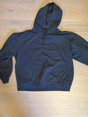 Marinblå  basic hoodie med huva - En enkel marinblå hoodie med huva och dragsnören. Modellen har ribbade muddar vid ärmslut och midja, samt en klassisk passform. Perfekt för en avslappnad och stilren look. Materialet känns mjukt och bekvämt mot huden.
