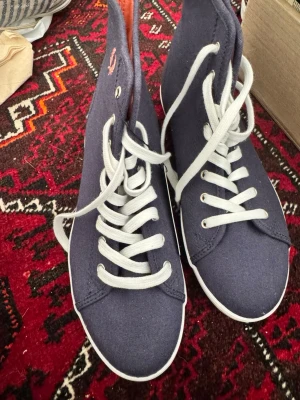 Blå canvas sneakers med högt skaft - Säljer ett par snygga sneakers i färgen carbon blue med vitt snörning och högt skaft. Skorna är gjorda i canvasmaterial och har en klassisk, stilren look som passar till många outfits.