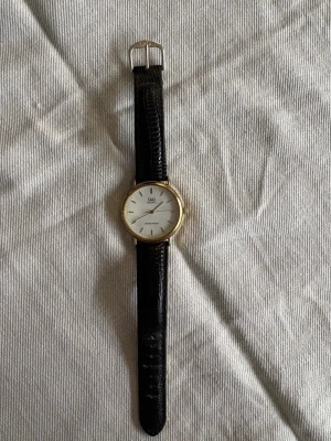 Q&Q klocka stilren med läderband - Q&Q klocka med japanskt kvartsurverk i fint skick med läderarmband. Uret mäter 35 mm. På uret står det ”Quartz ” och ”Water resist”.   Funktionstestad i flera dagar, håller tiden väl och med säljes nytt batteri. Läderarmbandet är lite slitet på ett ställe och bandhållarna har lossnat, annars ser klockan nästan nyut.   Säljes i befintligt skick.