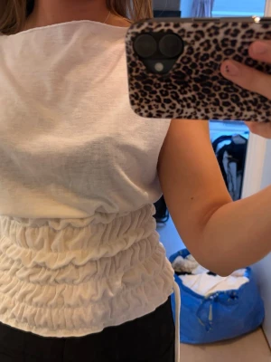 Vit ärmlös topp med rynkdetaljer - Från Shein. Säljer en vit ärmlös topp med bred halsringning och snygga rynkdetaljer i midjan. Toppen har en croppad passform och är gjord i ett mjukt bomullsliknande material. Perfekt för dig som vill ha en enkel men trendig look.