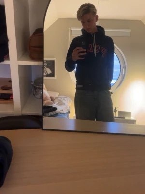 Mörkblå hoodie med POL-tryck - Säljer en mörkblå hoodie med huva och vita dragsnören. På bröstet står det 'POL' i stora röda bokstäver med vit kant. Hoodien har känguruficka framtill och ribbade muddar. Perfekt för en chill och avslappnad stil.