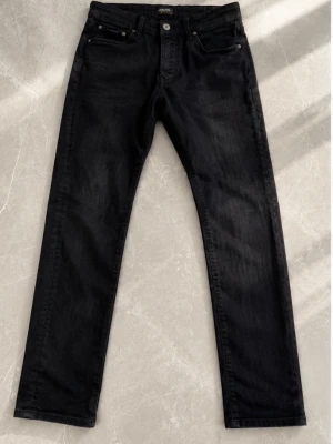 Svarta slim fit jeans - Säljer ett par svarta jeans med slim fit passform och klassisk femficksdesign. Jeansen har knappgylf och är tillverkade i ett mjukt denimtyg som ger en avslappnad look. Perfekta till en streetwear-outfit eller för en stilren vardagsstil.