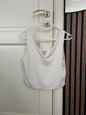Vit croppad linnetopp från Amisu - Säljer en enkel och stilren vit linnetopp från Amisu. Toppen är croppad och har en djupare rundad halsringning. Perfekt att matcha med jeans eller kjol för en clean look. Tillverkad i mjuk bomull för skön känsla.