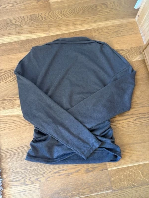 Mörkgrå långärmad tröja - En enkel och stilren mörkgrå långärmad tröja i mjukt material. Tröjan har en klassisk rak passform och rund halsringning. Perfekt att matcha med jeans eller kjol för en clean look.