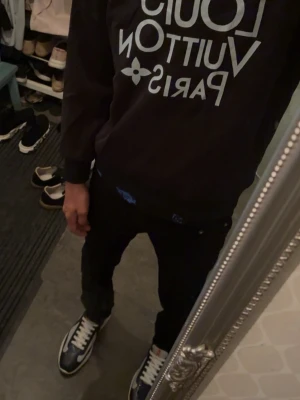 Svart hoodie med tryck  - Svart hoodie från med stort vitt Paris-tryck på bröstet och flera Paris-tryck på ryggen. Klassisk passform med långa ärmar och ribbade muddar. Perfekt för dig som gillar streetwear och exklusiva märken.
