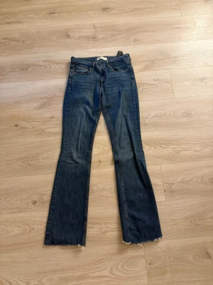Mörkblå bootcut jeans med rå kant - Säljer ett par mörkblå bootcut jeans med rå, fransad kant nedtill. Jeansen har klassisk femficksdesign och normal midja. Perfekta för en avslappnad och trendig look.