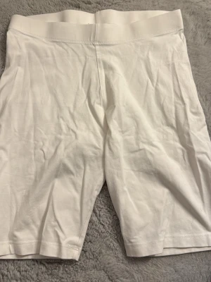 Vita cykelbyxleggings - Säljer ett par vita cykelbyxleggings med hög midja och elastisk linning. De är tillverkade i ett mjukt och stretchigt material som sitter skönt mot kroppen. Perfekta för en avslappnad och sportig look.