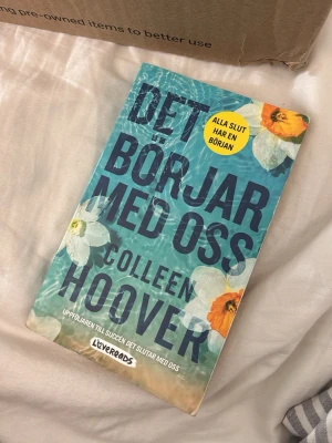 Det börjar med oss av Colleen Hoover - En svensk pocketbok av Colleen Hoover med titeln 'Det börjar med oss'. Omslaget är blått med blommor i vitt och orange, och texten är stor och tydlig. Boken är utgiven av Lovereads och är en uppföljare till 'Det slutar med oss'. Perfekt för dig som gillar romantik och drama.