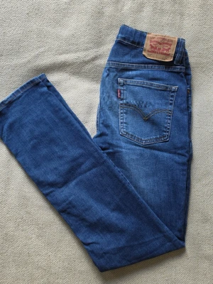 Levi’s 512 Slim Taper jeans blå storlek 16A / 176 cm / W28 L32 - Blå jeans från Levi’s i modellen 512 Slim Taper. Klassisk femficksmodell med smal passform, stretchig midja och avsmalnande ben. Mellanblå denim med tvättad look och klassiska Levi’s-detaljer.  Storlek 16A/176 cm Motsvarar ungefär W28 L32 512 Slim Taper  Bra begagnat skick med bruksslitage. Slitning på ena låret samt slitage och fransning vid bensluten, se bilder för detaljer.  Mått • Midja: ca 36 cm • Grenhöjd: ca 22 cm • Ytterbenslängd: ca 102 cm • Innerbenslängd: ca 81 cm • Benslut: ca 19 cm
