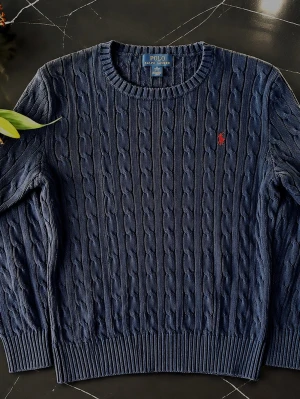 Polo Ralph Lauren Kabelstickad Tröja Navy Kids L / Granatowy Sweter - Klassisk Polo Ralph Lauren kabelstickad tröja i mörkblå/navy med den ikoniska broderade Polo Ralph Lauren-loggan ❤️💙  ✨ Detaljer: • Kabelstickad design • Mörkblå/navy • Rund hals • Broderad Polo Ralph Lauren-logga • 100 % bomull • Storlek Kids L  📏 Passform: Kids L – passar ungefär XS–S / EU 34–36 beroende på önskad passform. Hör gärna av dig om du vill ha exakta mått!  ✅ Skick: Mycket fint skick. Inga hål, fläckar eller andra anmärkningar.  En stilren och lättmatchad tröja som passar perfekt 