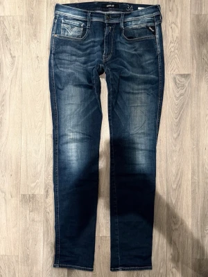 Replay Anbass Hyperflex Mörkblå W34/L34 - Slim Fit - Replay Anbass Hyperflex mörkblå jeans med slim fit-passform som sitter smalt och bekvämt och funkar till allt, storlek W34/L34, midja 42,5 cm, ytterbenslängd 109,5 cm, benöppning 16,5 cm, modellen är 185cm & väger 65kg, lite slitna i skrevet, i övrigt i fint skick.