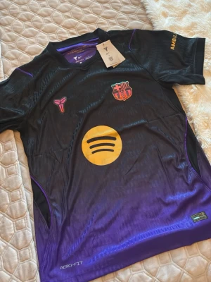 FC Barcelona x Kobe Bryant Nike tröja 2026/2027 - Säljer en svart och lila FC Barcelona x Kobe Bryant matchtröja från Nike med Aero-Fit material. Tröjan har klubbmärke, Kobe-logga och Spotify-logga på bröstet samt citat från Kobe Bryant i nacken. Perfekt för dig som älskar fotboll och basket. modell 2026/2027 storlek L men slim fit passar M med!
