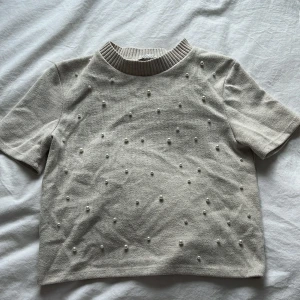 Beige stickad pärltröja från Zara - Superfin beige stickad tröja från Zara med korta ärmar och ribbad hals. Tröjan har pärlor över hela framsidan och är fint skick! 