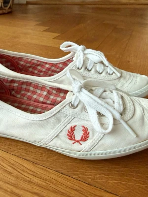 Fred Perry skor - Vita tygskor från Fred Perry. Strl 37,  Korallfärgad logotype och korallfärgade / rutiga på insidan.   Hämtas i Nacka eller skickas mot porto. 