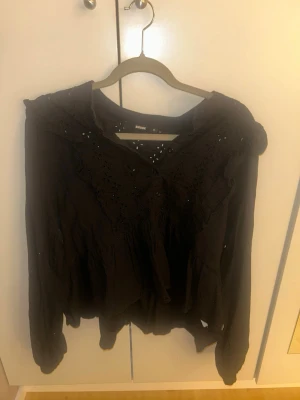 Svart blus med spetsdetaljer - Säljer en svart blus med långa ärmar och fina spetsdetaljer över axlar och bröst. Blusen har en lös passform och v-ringning. Perfekt för dig som gillar en bohemisk och avslappnad stil.
