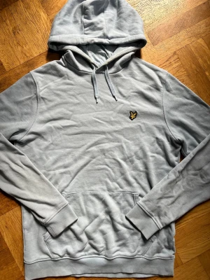 Ljusblå lyle scott hoodie  - Snygg ljusblåhoodie med huva och dragsnören. Har en broderad gul och svart logga på bröstet och en klassisk magficka framtill. Tillverkad i mjukt material och har ribbade muddar vid ärmar och nederkant. Perfekt för en chill och avslappnad stil. Liten missfärgning som jag visar på bilden vid luvan annars bra skick. Storlek M. Det är bara att höra av dig vid frågor!!🙋‍♂️