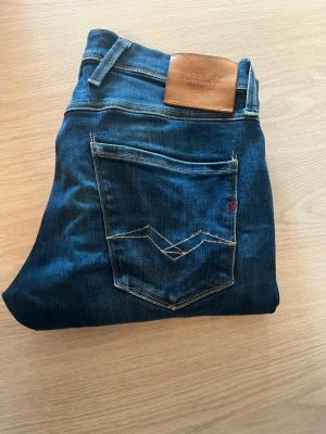 Replay Hyperflex jeans - Snygga blå jeans från Replay Hyperflex med klassisk femficksmodell och kontrastsömmar. Jeansen har en skinnpatch med logga bak i midjan och en diskret röd detalj på bakfickan. Materialet är stretchigt för extra komfort och passform. Priset är ej hugget i sten