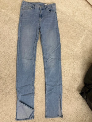 Ljusblå jeans  - Säljer ett par ljusblå skinny jeans med slitsar nertill på benen. Jeansen har klassisk femficksdesign, hög midja och är i stretchigt denimtyg.