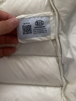 Vit dunjacka från Parajumpers - Snygg och varm vit dunjacka från Parajumpers med huva och långa ärmar. Jackan har quiltad design, dragkedja och knappar framtill samt praktiska fickor på sidorna. Perfekt för kalla vinterdagar och riktigt stilren look.