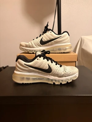Nike vita sneakers med svart swoosh - Nike sneakers i vitt meshmaterial med svart swoosh på sidan och svarta skosnören. Skorna har en synlig luftsula och svart yttersula. Låg modell med ventilerande ovandel och bekväm dämpning. Perfekta för dig som gillar sportig och clean stil.
