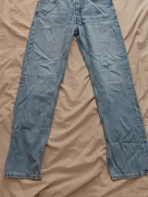 Ljusblå jeans - Säljer ett par ljusblå jeans med rak passform och klassisk femficksdesign. Jeansen har hög midja och är tillverkade i denim med synliga sömmar. Perfekta för en avslappnad och trendig look.