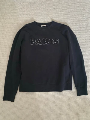 Svart sweatshirt med PARIS-tryck - Supersnygg sweatshirt med ”Paris” tryck från Sandro Paris. Inga defekter. Säljer då den ej kommer till användning. Står ingen storlek men skulle säga att den är i S/M💞