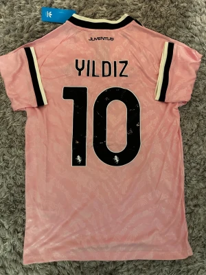 Juventus bortatröja, Yildiz 10 - Säljer en rosa Juventus matchtröja med Yildiz och nummer 10 på ryggen. Tröjan har svarta detaljer, Jeep-logga på framsidan och Adidas-märke. Tröjan är helt ny i storlek M