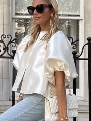 Vit blus med puffärmar  - Supersnygg vit blus i glansigt satinmaterial med stora puffärmar och rak passform. Blusen har rund halsringning och stängs framtill med dolda knappar. Perfekt för dig som vill sticka ut med en trendig och elegant look.