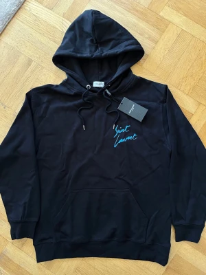 Svart hoodie från Saint Laurent - Svart hoodie från Saint Laurent som är helt ny i storlek S, med blå stilig logga på bröstet. 