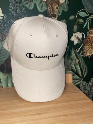 Champion keps - Snygg beige keps från Champion med böjd skärm och justerbar rem bak. Helt oanvänd och ny med pris lapp.