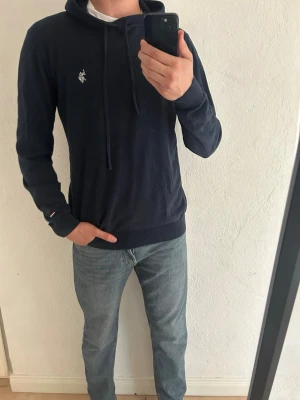 Mörkblå Ralph lauren hoodie  - Snygg mörkblå hoodie med dragsko i huvan och en liten vit broderad logga på bröstet. Modellen har ribbade muddar vid ärmslut och nederkant. Perfekt för en avslappnad och stilren look. Märket är U.S.POLO ASSN
