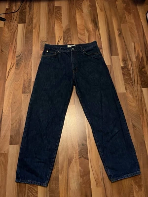 Mörkblå raka jeans från Woodbird - Säljer ett par mörkblå jeans från Woodbird med rak passform och klassisk femficksdesign. Priset går att pruta ner vid snabb affär!! Jeansen har gulbruna sömmar och är tillverkade i slitstark denim. Perfekta för dig som gillar en enkel, dom är ganska lösa i fitten. Skriv om funderingar!😃