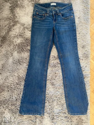 lågmijade jeans med fick dettaljer  - Säljer ett par klassiska blå bootcut jeans. Jeansen har knapp- och dragkedjestängning samt dekorativa ficklock med knappar bak. Perfekta till sneakers eller boots för en avslappnad look.