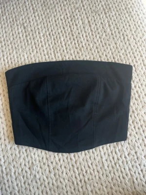 Svart tubtopp med dragkedja - Säljer en stilren svart tubtopp med dragkedja i ryggen. Toppen har en enkel och clean design som sitter tight runt överkroppen. Perfekt att matcha med höga jeans eller kjol för en trendig look.