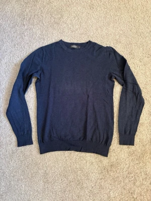 Dressmann Supima Cotton Stickad Tröja - Marinblå finstickad tröja från Dressmann i Supima Cotton. Klassisk modell som passar perfekt över en skjorta eller tillsammans med jeans och chinos. Använd men i mycket fint skick.  • Storlek S • Supima Cotton • Mycket bra skick  📦 Skickas snabbt.