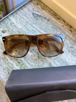 Bruna Wayfarer solglasögon Ray-Ban - Snygga Wayfarer solglasögon från Ray-Ban i brun transparent plast med klassisk form. Glasen är tonade i brunt och bågarna har små silverdetaljer vid hörnen. Perfekta för soliga dagar och ger en cool retrovibe.