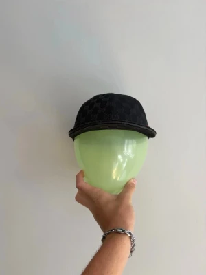 Svart keps     - Säljer en svart keps  med klassiskt mönster över hela kepsen. som ger en ikonisk touch. Kepsen har böjd skärm och justerbar rem bak. Perfekt för dig som vill ha en stilren och lyxig accessoar.