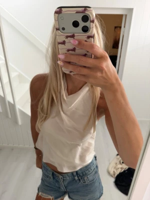 Vit ärmlös halterneck topp - Säljer en stilren vit halterneck topp med öppen rygg och croppad passform. Toppen är ärmlös och har en mjuk, lätt tygkänsla som passar perfekt till sommaren. Enkel att matcha med jeans eller kjol för en fräsch look.