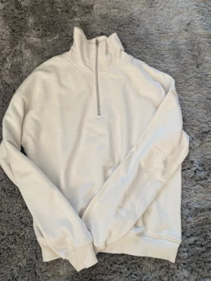 Vit half-zip hoodie - Säljer en stilren vit hoodie med half-zip och hög krage. Tröjan har långa ärmar, ribbade muddar och är gjord i mjukt sweatshirtmaterial. Perfekt för en clean och avslappnad look.