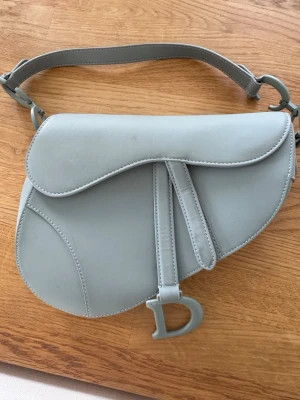 Grå väska - Vacker CD-väska med lätt slitage på hårdvaran, se bilderna för detaljer. Matt grå färg.  Mått:  * Bredd: 24 cm * Höjd: 19 cm