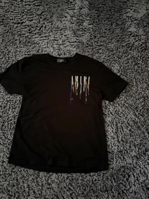 Svart AMIRI t-shirt med färgstänk - Säljer en svart t-shirt från AMIRI. Storlek S. Hör av dig om du har frågor.