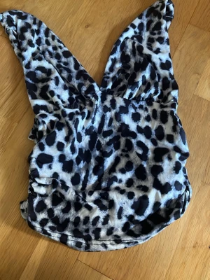 Leopardmönstrad baddräkt med v-ringning - Snygg baddräkt med leopardmönster i svart, grått och vitt. Djup v-ringning framtill och breda axelband ger en trendig look. Materialet känns stretchigt och följsamt, perfekt för strand eller pool. Baddräkten har lätt rynkade sidor för en smickrande passform.