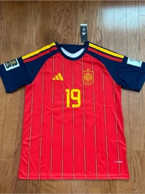 Lamine Yamal Spanien vm 2026 matchtröja  - Säljer en röd och marinblå matchtröja från Spaniens landslag med gula detaljer och nummer 19, Lamine Yamal på ryggen. Tröjan har korta ärmar, tunnt funktionsmaterial och officiella tryck på bröst och ärmar. Perfekt för dig som älskar fotboll och vill stötta Spanien.