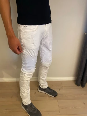Vita slim fit jeans med slitningar - Snygga vita slim fit jeans med slitna detaljer på framsidan. Jeansen har klassisk femficksdesign och smal passform som sitter tajt längs benen. Perfekta för dig som vill ha en fräsch och trendig look.