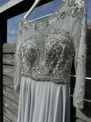 Klänning till fest/bal/examen/bröllop - Klänning från Terani Couture till festlig tillställning, bröllop eller bal exempelvis. Inköpt i Jönköping på Diamar Brud och Fest, för 7999kr nypris.   Klänningen har massvis med fina detaljer, stenar, paljetter, strass och pärlor samt att den faller fint. Öppen del i ryggen som också är en fin detalj. Ryggen sluts med dragkedja och även med knäppe upp mot nacken. Klänningen har insydda stadiga kupor för bysten som gör den väldigt bekväm att bära. Färgen är silvergrå. Kemtvättad och utan fläckar