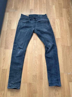 Svarta slim fit jeans dondup - Snygga svarta slim fit jeans med diskreta slitningar och unika sömdetaljer på bakfickorna. Klassisk femficksmodell med knappgylf och bälteshällor. Perfekta för dig som gillar en stilren men ändå cool look.