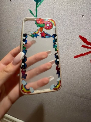 Färgglatt genomskinligt mobilskal - Säljer ett genomskinligt mobilskal med färgglada dekorationer som glass, donut, stjärnor, blixtar och regnbågar. Skalet har en lekfull och unik design som verkligen sticker ut. Passar dig som vill ha ett personligt och kreativt mobilskal. Passar till både en IPhone 11 och en XR. 