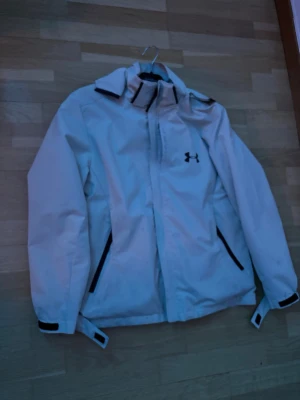 Under Armour vindjacka - Hej! Säljer denna fina jacka från under armour som är perfekt nu inför slutet av sommaren och hösten. Den är endast använd ett par gånger då jag har skiftat mellan denna och en annan. Men nu bestämt mig för att sälja den. Den är i mycket fint skick och det finns inga defekter. Hör av er om mer bilder eller frågor!